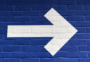 White arrow on a blue brick wall pointing forward, toward finding meaning.