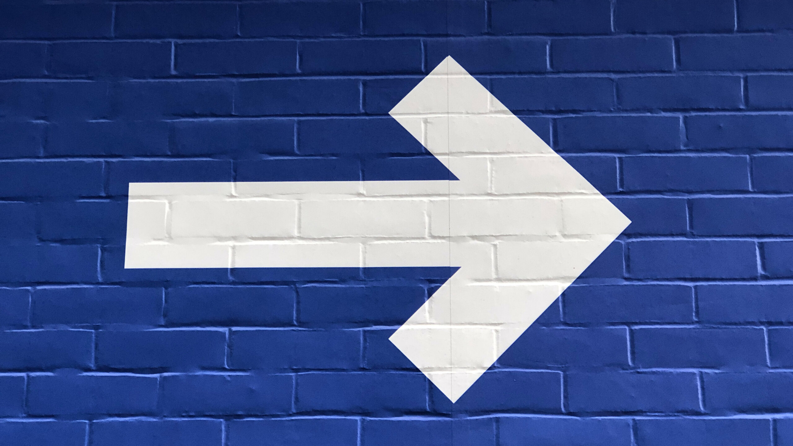 White arrow on a blue brick wall pointing forward, toward finding meaning.